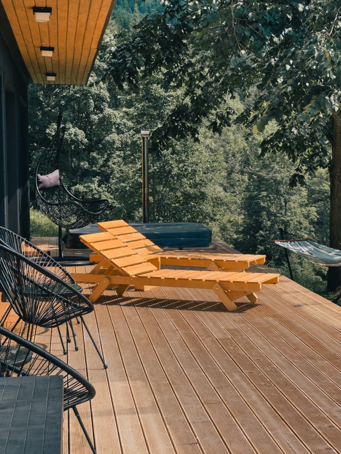 Home Wooden deck with lounge chairs surrounded by lush greenery, perfect for relaxation.