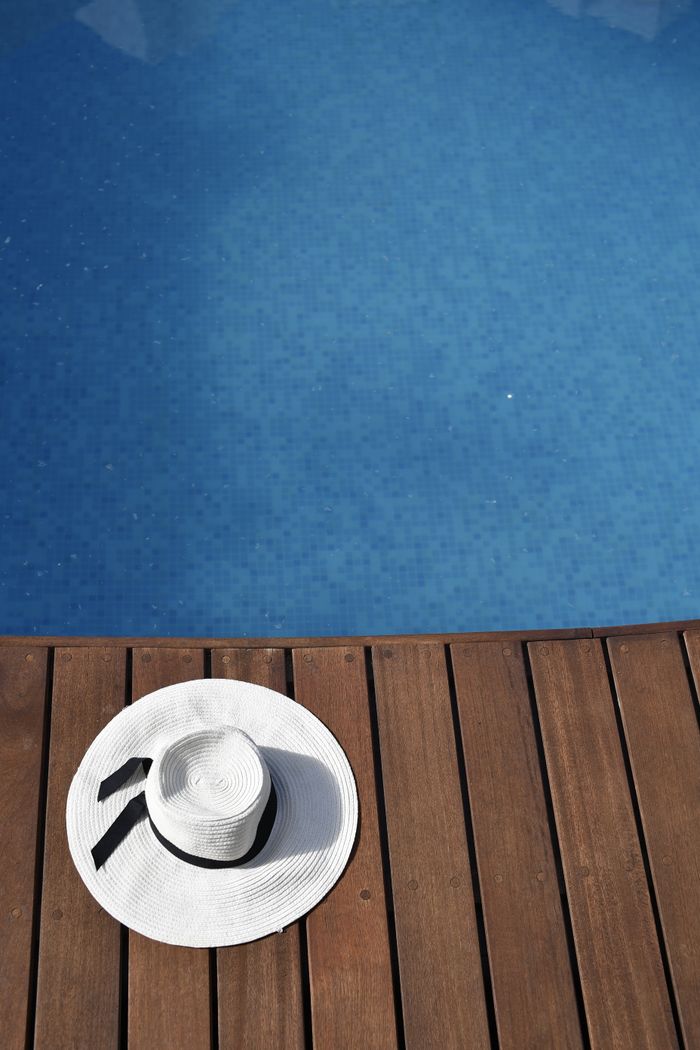 Mastering the First Impression: Your intriguing post title goes here A white sun hat rests on a wooden deck by a clear blue pool in Cancun, Mexico, capturing relaxation and summer vibes.